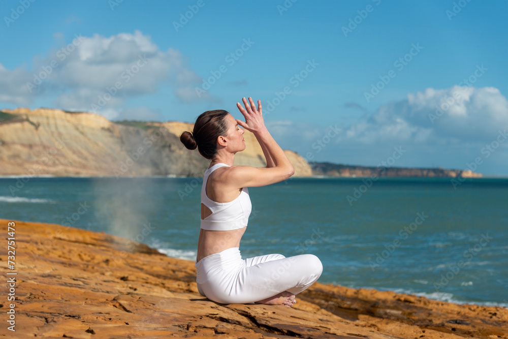 sporty woman practicing yoga and meditating on rocks by the sea.