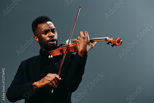 African American man playing violin in black suit on gray background, artistic music performance concept