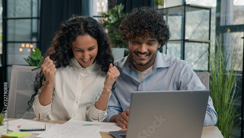 Multiracial business partners multiethnic colleagues Indian businessman and Arabian businesswoman working together paperwork in office happy team celebrate success achievement win startup on laptop