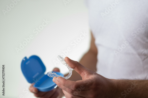 close-up of a young man hands holding transparent dental retainer and a case for their storage and protection. Male hands holding dental teeth aligner, copy space, isolated on light grey color