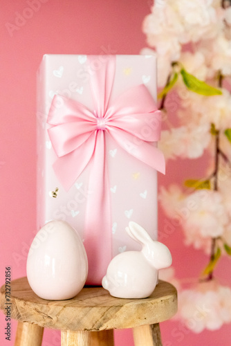 Porcelain Easter egg, bunny, gift box, wooden stool on a pink background.