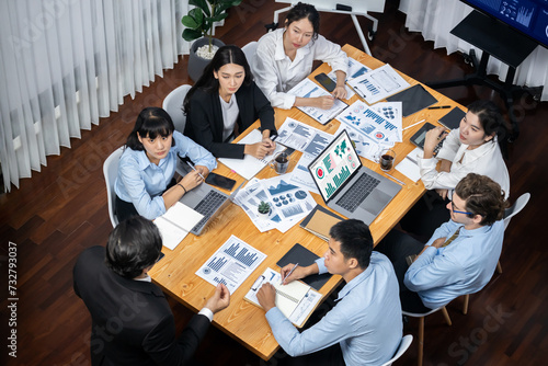 Wide top view of diverse group of business analyst team analyzing financial data report paper on meeting table. Chart and graph dashboard by business intelligence analysis. Meticulous