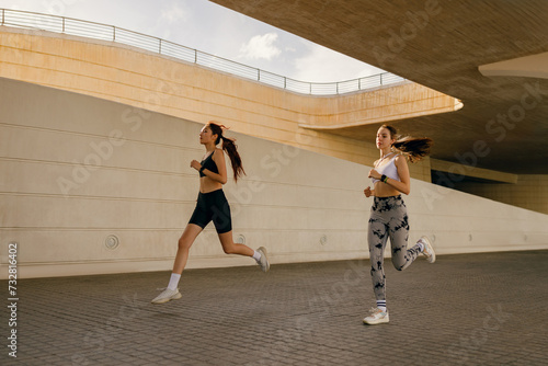 Two young women in sportswear are running on modern buildings background. Active lifestyle concept