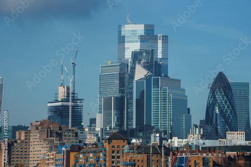 Daytime view of London's financial district with the iconic Gherkin, underconstruction skyscrapers, and a mix of modern buildings under a clear sky. No Christmas elements present.