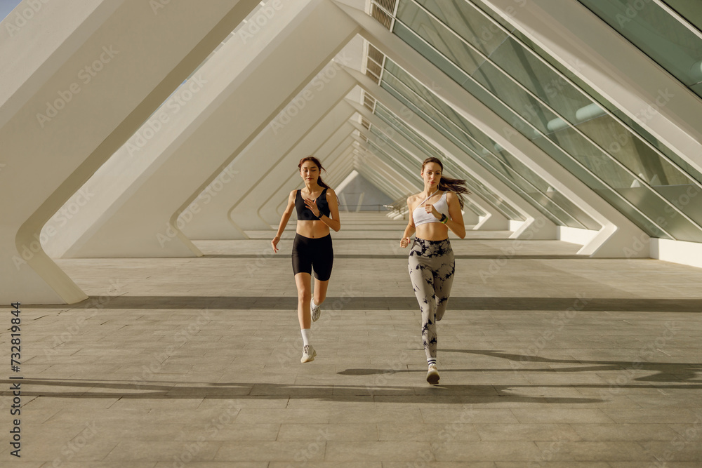 Two athletic women in sportswear is jogging around the city in early morning. Reaching the goal Two athletic women in sportswear is jogging around the city in early morning. Reaching the goal