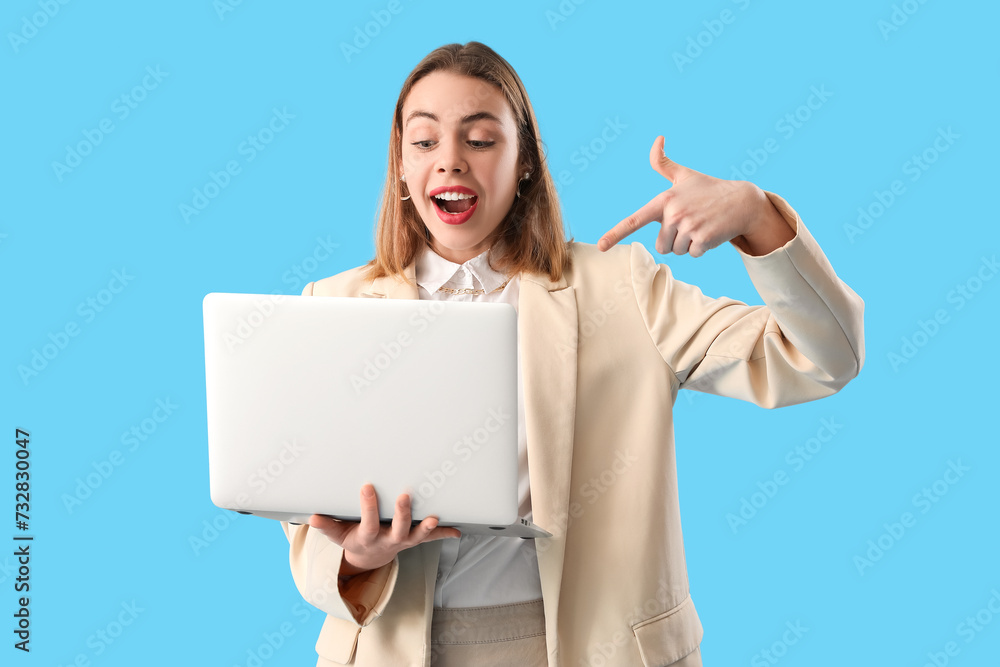 Surprised female programmer pointing at laptop on blue background Surprised female programmer pointing at laptop on blue background