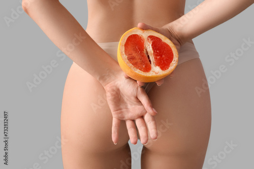 Woman with half of grapefruit on light background, back view. Sex concept photo
