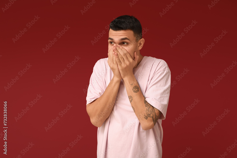Handsome ashamed young man covering face with hands on red background Handsome ashamed young man covering face with hands on red background