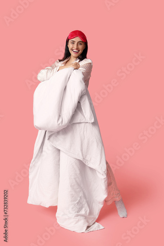 Pretty young woman with blanket and sleeping mask on pink background