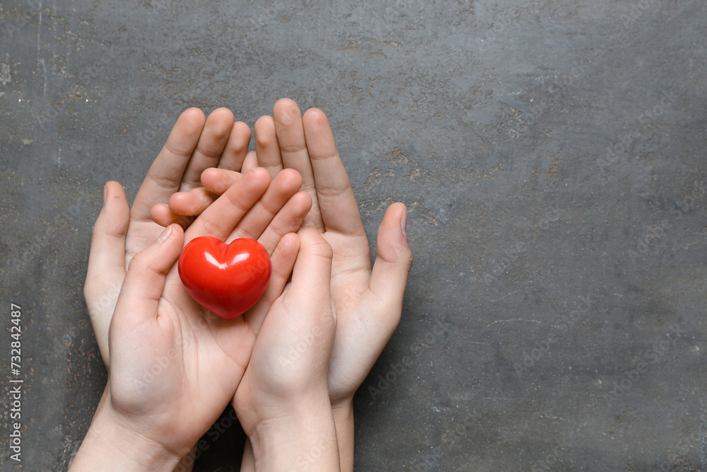 Hands of woman and child with red heart on black background