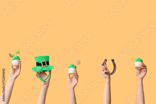 Female hands with tasty cupcakes, leprechaun hat and horseshoe for St. Patrick's Day on beige background