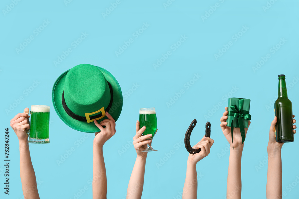 Female hands holding beer and party decor for St. Patrick's Day celebration on blue background Female hands holding beer and party decor for St. Patrick's Day celebration on blue background