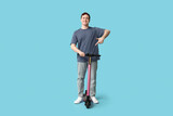 Young man pointing at modern electric kick scooter on blue background