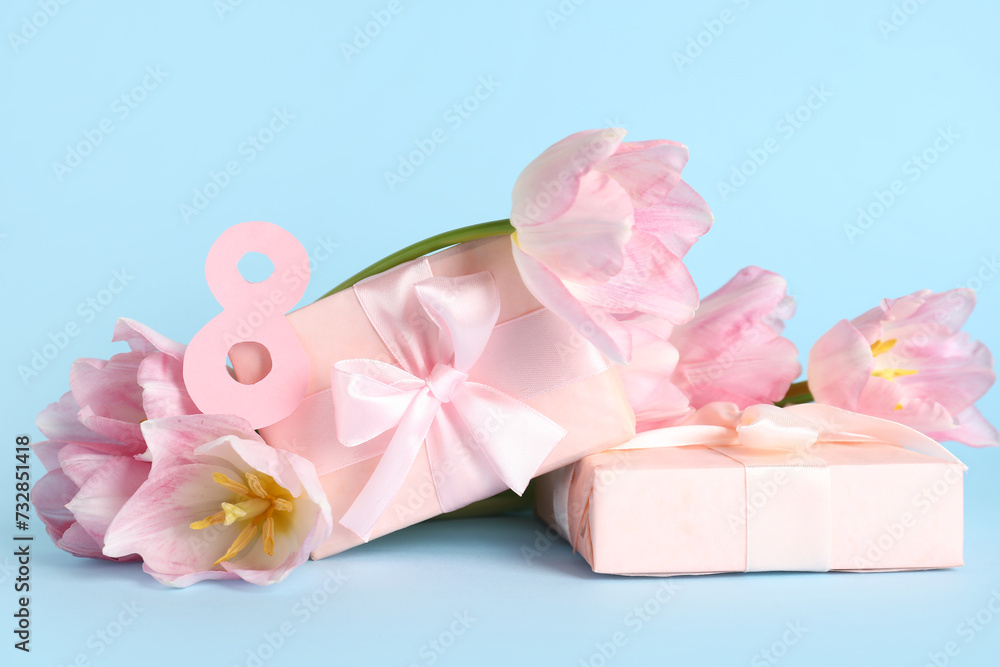 Figure 8 made of paper with gift boxes and beautiful pink tulips on blue background. International Women's Day