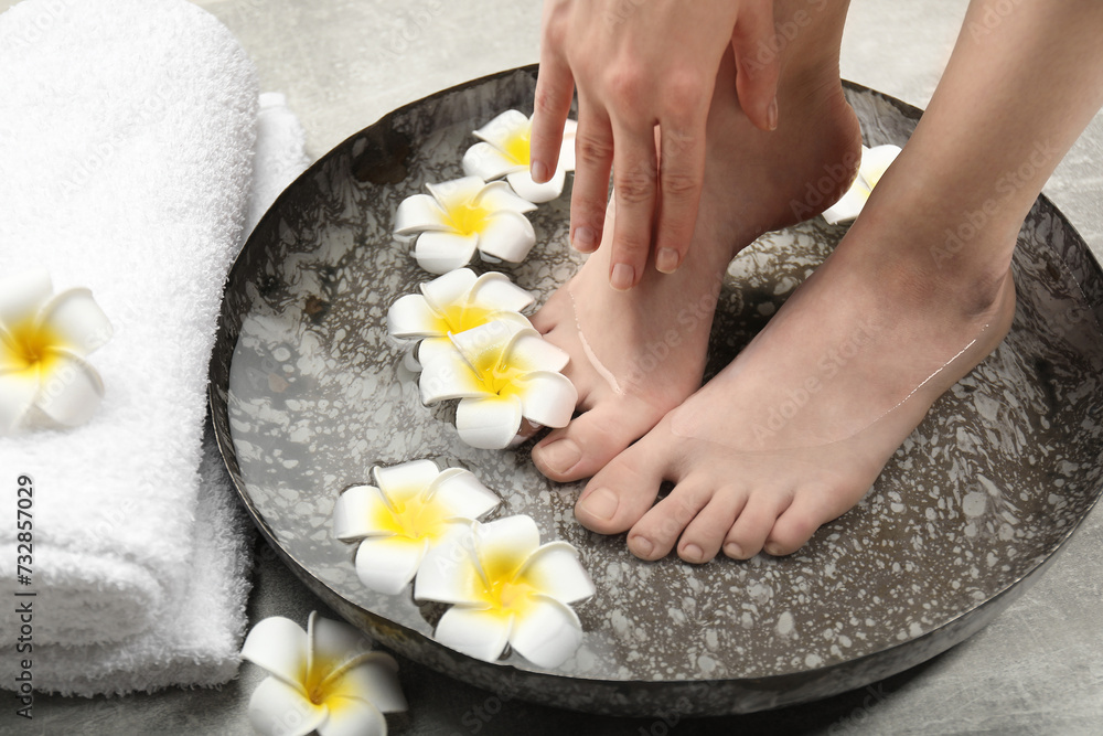 Woman soaking her feet in bowl with water and flowers on floor, closeup. Spa treatment Woman soaking her feet in bowl with water and flowers on floor, closeup. Spa treatment