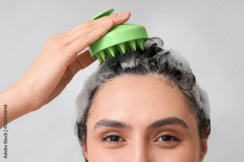 © Pixel-Shot - Beautiful young woman using hair scalp massager on grey background, closeup