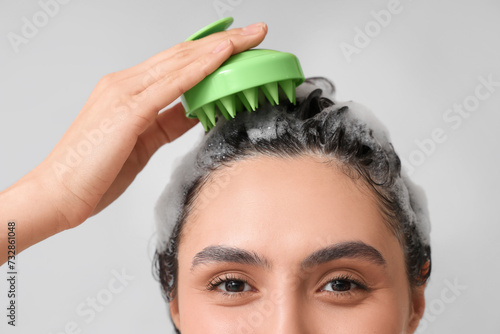 Beautiful young woman using hair scalp massager on grey background, closeup photo