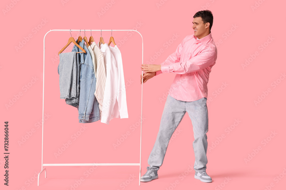 Handsome young happy man and rack with stylish clothes on pink background Handsome young happy man and rack with stylish clothes on pink background
