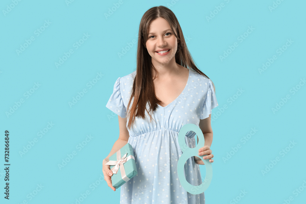 Beautiful young pregnant woman with figure 8 made of paper and gift box on blue background. International Women's Day Beautiful young pregnant woman with figure 8 made of paper and gift box on blue background. International Women's Day