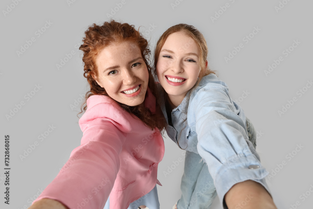 Stylish redhead sisters taking selfie on grey background Stylish redhead sisters taking selfie on grey background