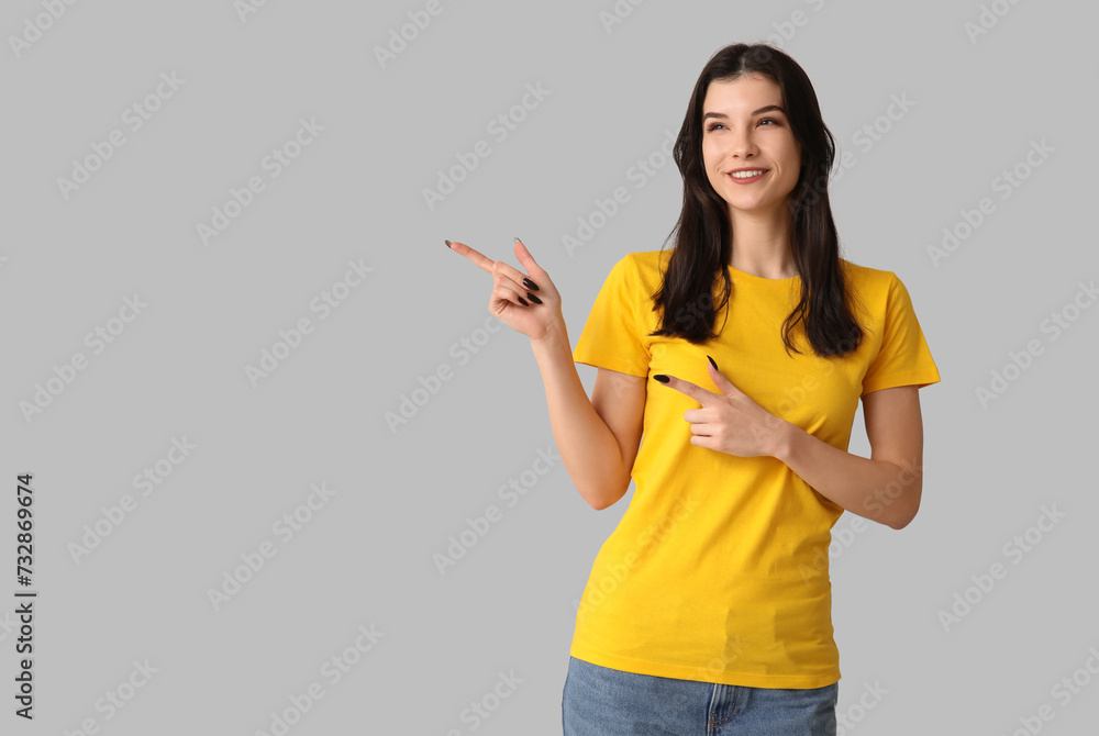 Young woman in stylish yellow t-shirt pointing at something on grey background Young woman in stylish yellow t-shirt pointing at something on grey background