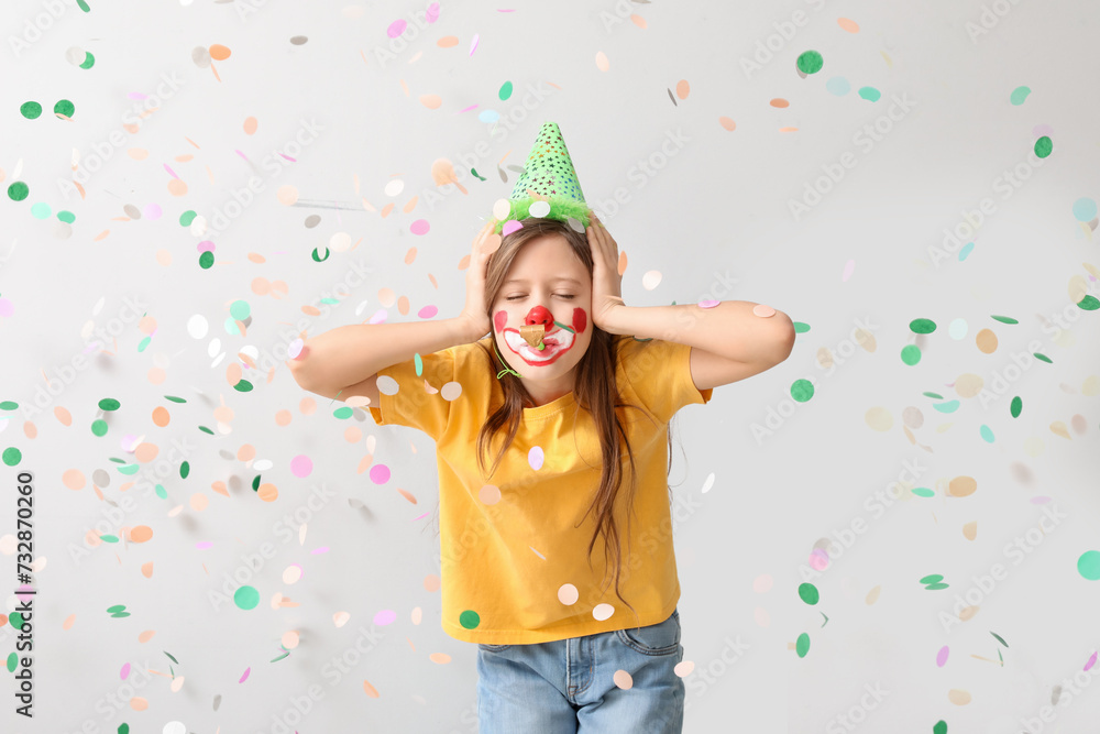 Funny girl with clown makeup, party hat, whistle and confetti covering ears on white background. April Fool's Day celebration