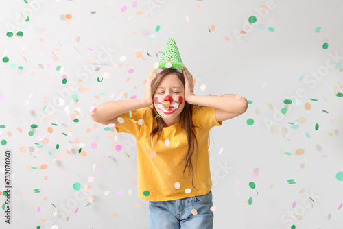 Funny girl with clown makeup, party hat, whistle and confetti covering ears on white background. April Fool's Day celebration