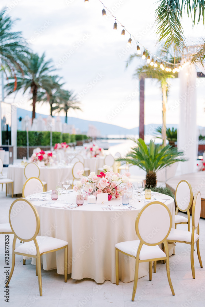 White chairs stand around a round festive table with a bouquet of flowers
