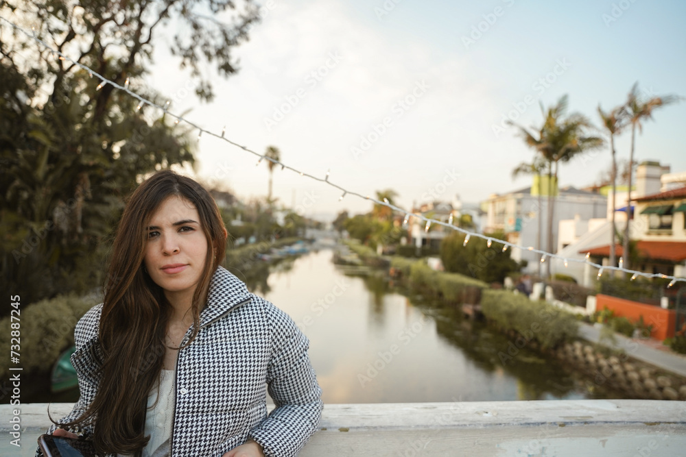 Photo of a gorgeous young woman tourist in Venice Canals, Los Angeles, California, during the sunset