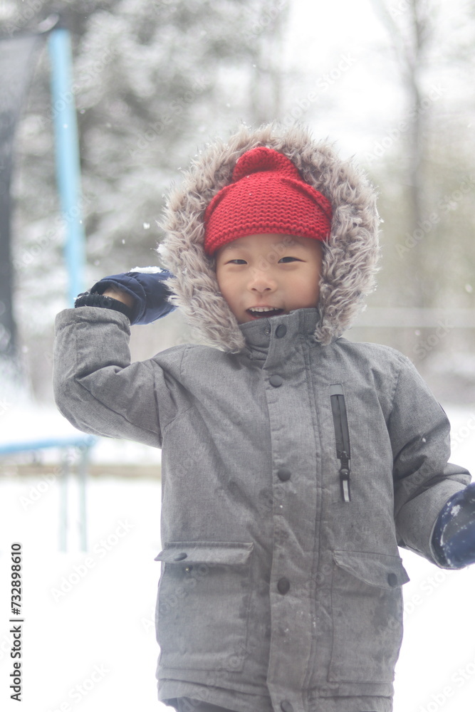 a child with a red hat and jacket playing snowball fight