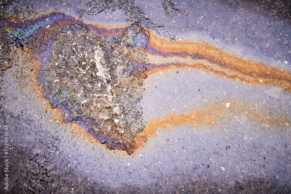 A bright spot of oil or gasoline splash on the asphalt after the snow melts A bright spot of oil or gasoline splash on the asphalt after the snow melts