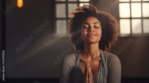 Mature woman meditating with her eyes closed and her hands in prayer position. Black woman with dreadlocks practicing yoga in a studio. Happy middle-aged woman maintaining a healthy lifestyle photo