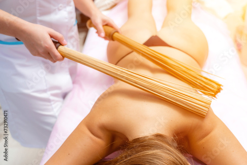 Woman masseuse doing double samurai massage with bamboo brooms in spa. Relaxing massage concept photo