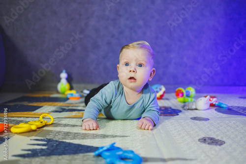 A 4-month-old boy lies on a mat and crawls. The baby lies on a thermal mat and plays. Self-development of a newborn child. Toys for child development.