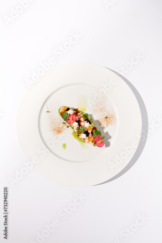 Elevated view of avocado with shrimp tartare, mango, cream cheese, and black caviar on a white plate