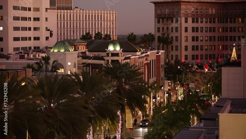 Twilight view of traffic streaming down Rodeo Drive with historic downtown skyline of Beverly Hills, California, USA.