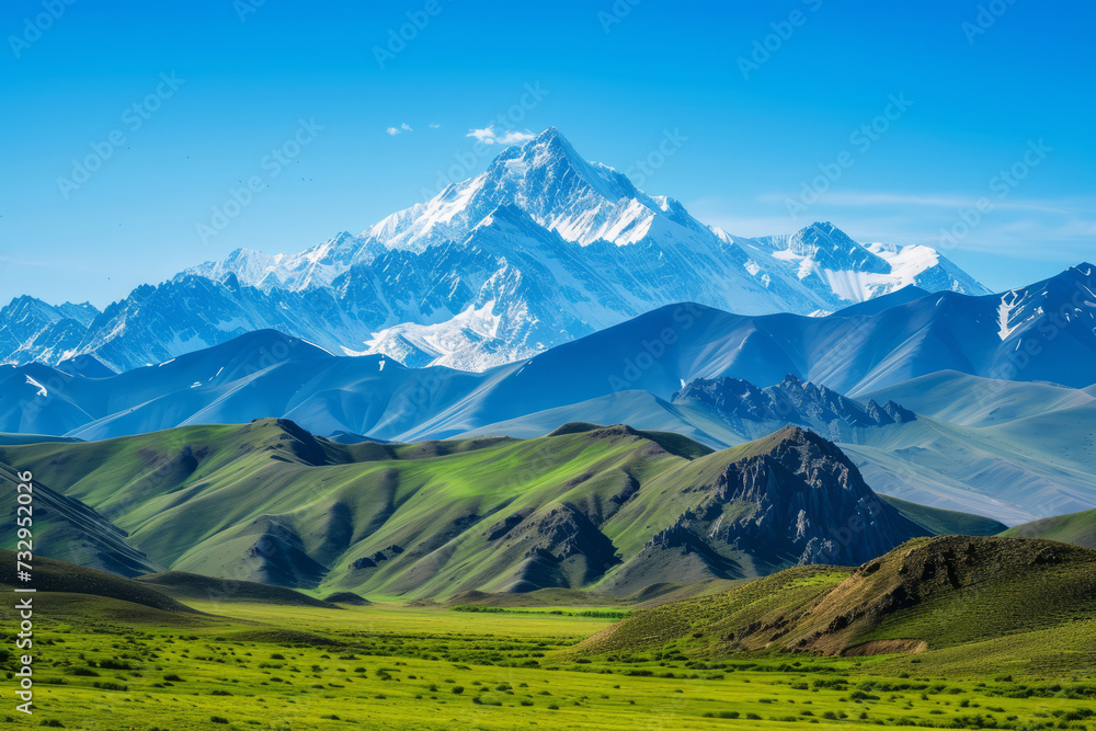 Majestic Snow-Capped Mountain Range Overlooking Green Valleys, Snow-capped peaks rise majestically above vibrant green valleys under the clear blue sky, offering a breathtaking natural landscape.