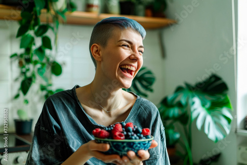 Joyful woman with short blue hair having breakfast eating a bowl of wild berries, healthy food and lifestyle photo