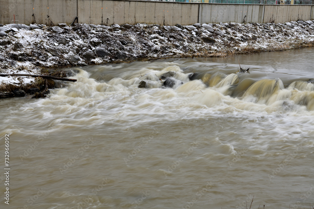 City river milky view between protective walls with a small waterfall