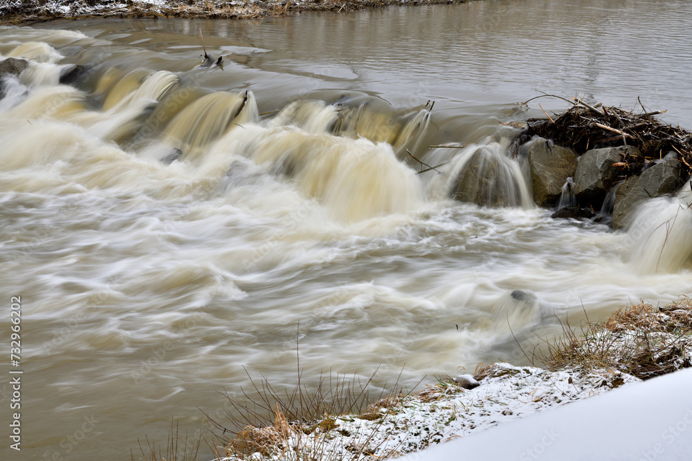 City river milky view between protective walls with a small waterfall