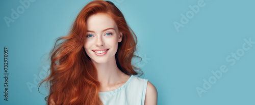 Portrait of an elegant, sexy smiling woman with perfect skin and long red hair, on a light blue background, banner.