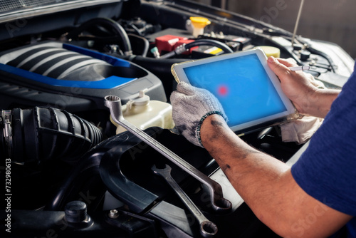 The mechanic checks the engine using tablet computer technology. Complete with wrench tool Auto mechanic working in the garage. Repair service.