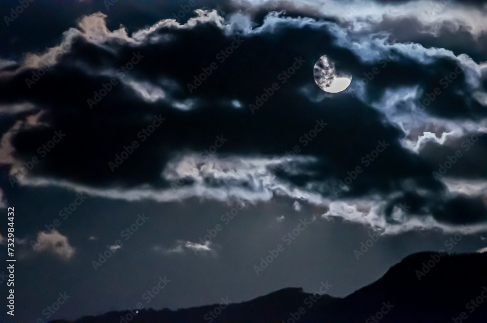 Luna piena coperta dalle nuvole con profilo di montagne