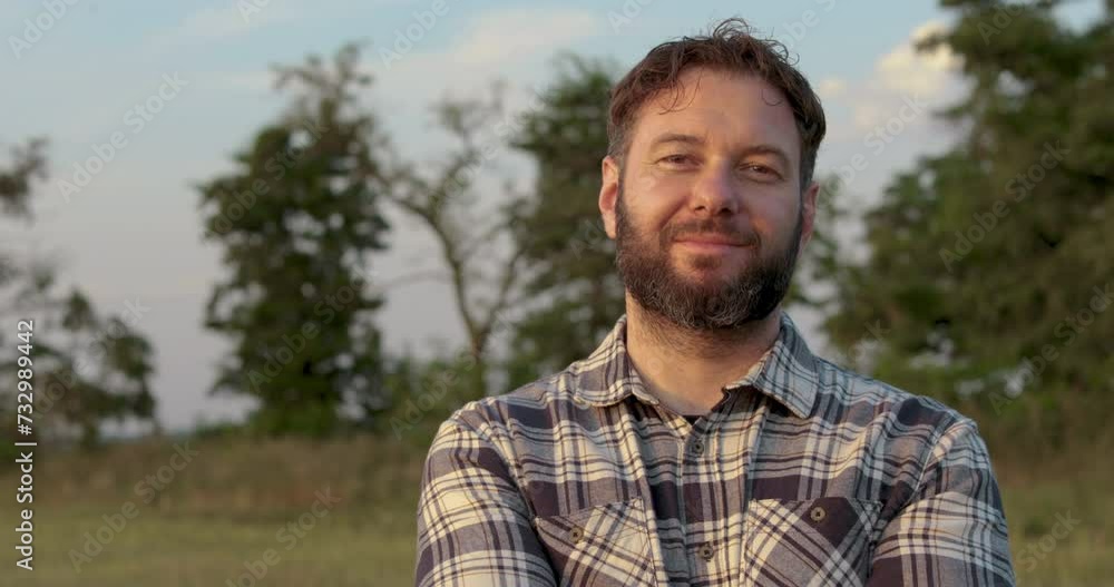 Portrait of a male farmer standing outdoors in a field. A man in a checkered shirt. Cheerful farmer crossing his arms. Agricultural business. Portrait of a male farmer standing outdoors in a field. A man in a checkered shirt. Cheerful farmer crossing his arms. Agricultural business.