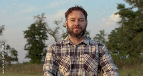 Portrait of a male farmer standing outdoors in a field. A man in a checkered shirt. Cheerful farmer crossing his arms. Agricultural business.