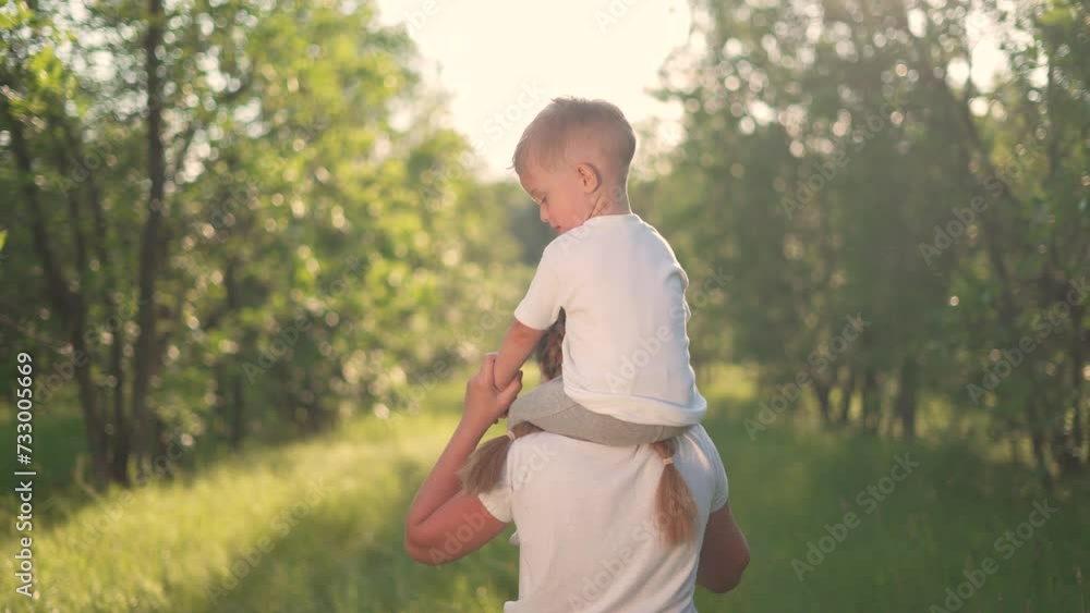 Happy family concept. children relax in a forest park at sunset. children's friendship.baby sits on his sister's shoulders. games in forest park outdoors.happy children walking together on green grass Happy family concept. children relax in a forest park at sunset. children's friendship.baby sits on his sister's shoulders. games in forest park outdoors.happy children walking together on green grass