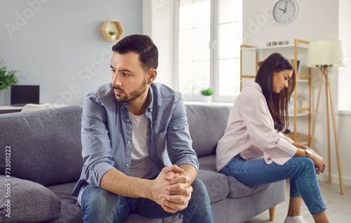 Disappointed couple sitting on sofa back to back, facing away from each other. Portrait of frustrated husband and wife feeling upset after argument and making decision of breaking up get divorced photo