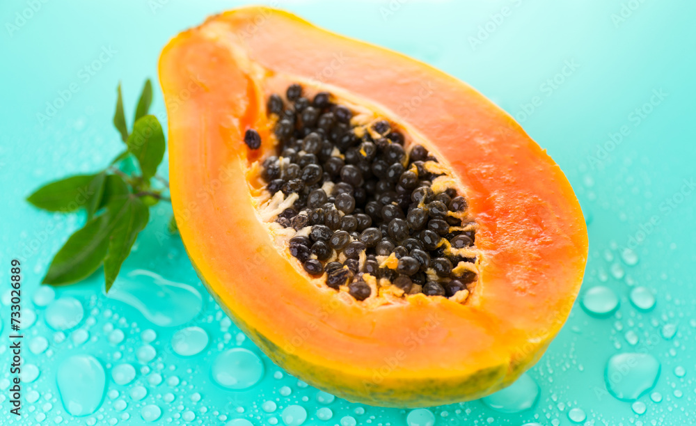 Papaya fruit on blue background with water drops, fresh exotic fruits design. Half of fresh organic ripe Papaya exotic fruit with leaf close up Papaya fruit on blue background with water drops, fresh exotic fruits design. Half of fresh organic ripe Papaya exotic fruit with leaf close up