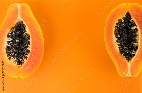 Papaya fruits on orange, yellow background. Halved fresh organic Papaya exotic fruit border design, close up. Top view. 