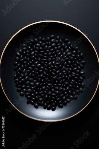 A photo of black beans neatly arranged on a gold plate placed on a black background.